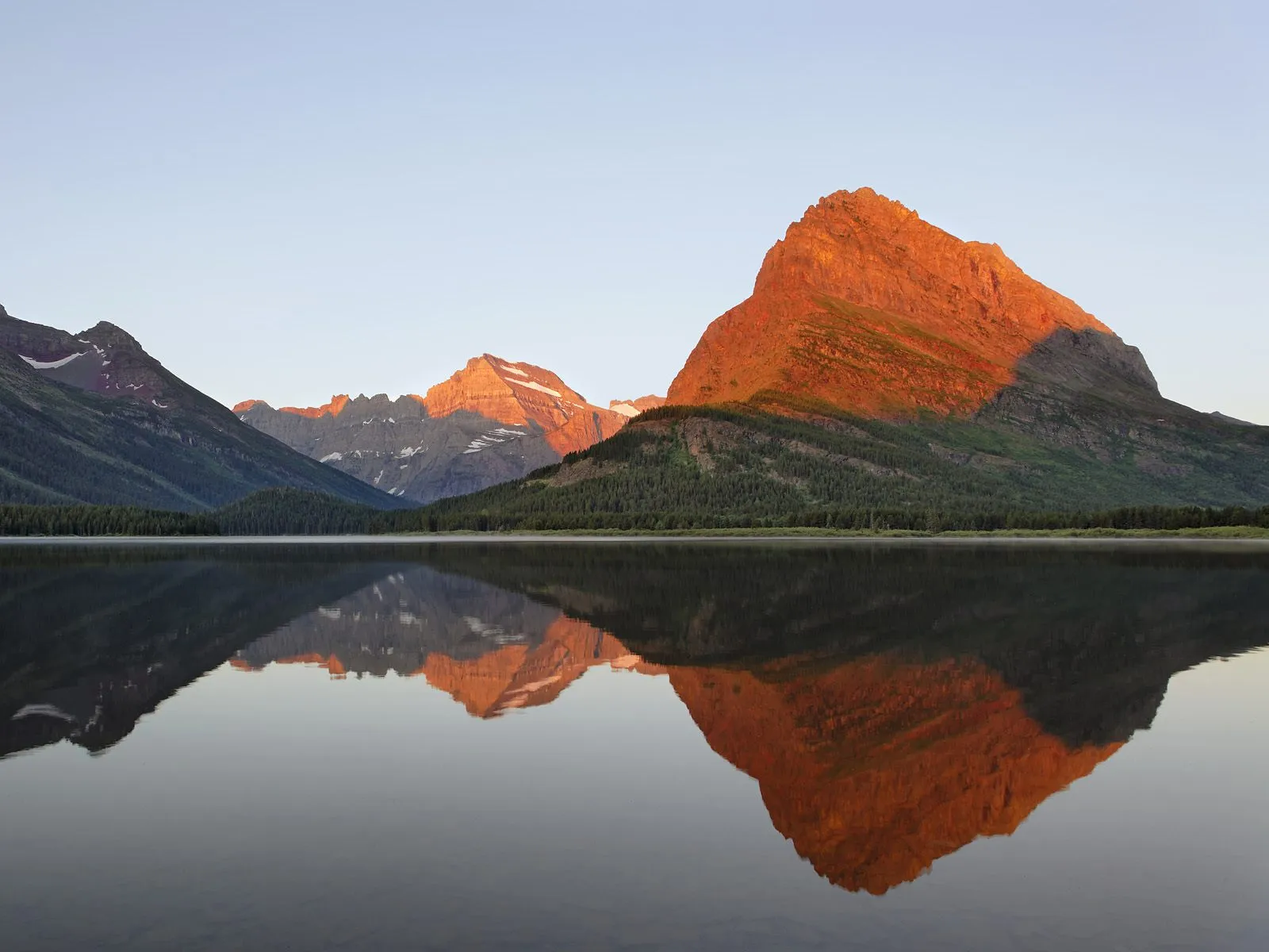 Sunrise light illuminates mountain peaks reflected in a calm lake.
