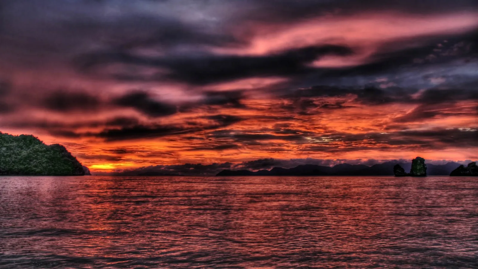 A vibrant sunset over a tropical ocean with islands.