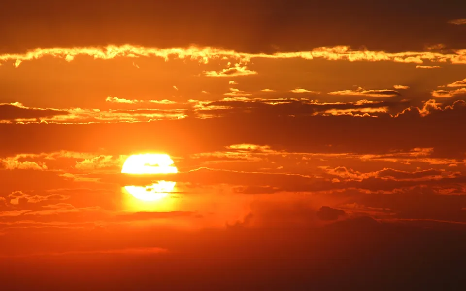The sun is setting behind a layer of clouds, casting a warm orange and yellow glow across the sky.