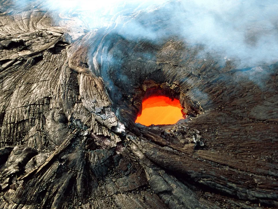 A close-up view of a volcanic crater with glowing orange lava and white smoke.