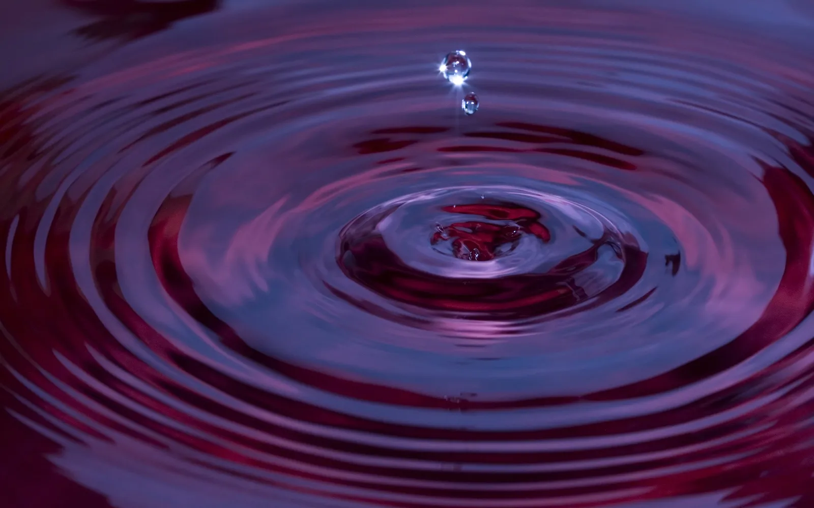 A close-up of a water drop falling into purple liquid, creating concentric ripples.