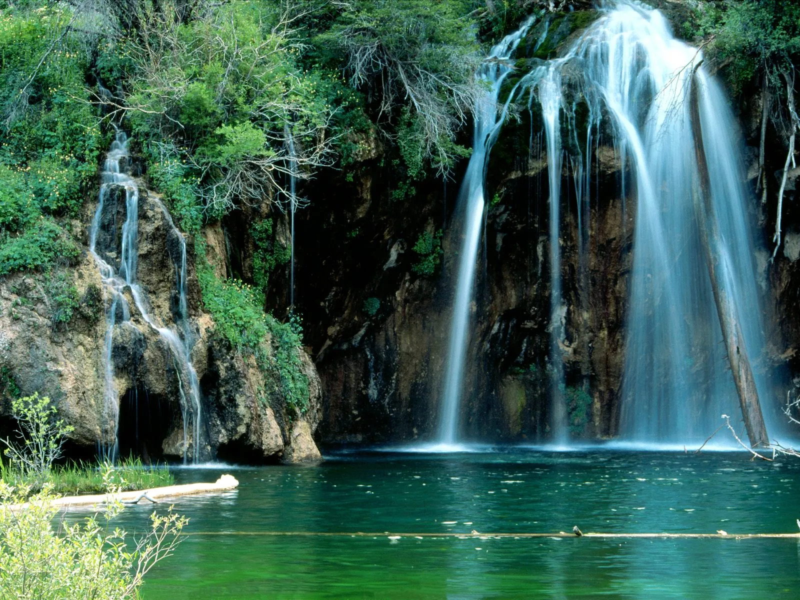 A wide waterfall cascades down a rocky cliff into a vibrant green pool of water.
