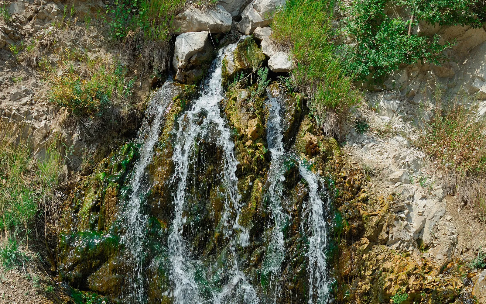 A small waterfall cascades down a rocky cliff face covered in moss and green vegetation.
