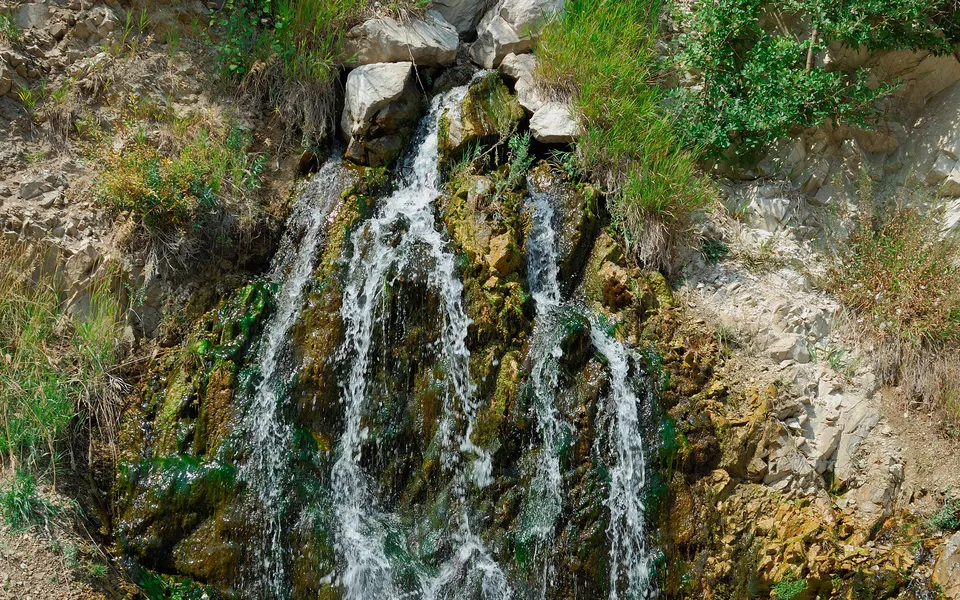 A small waterfall cascades down a rocky cliff face covered in moss and green vegetation.
