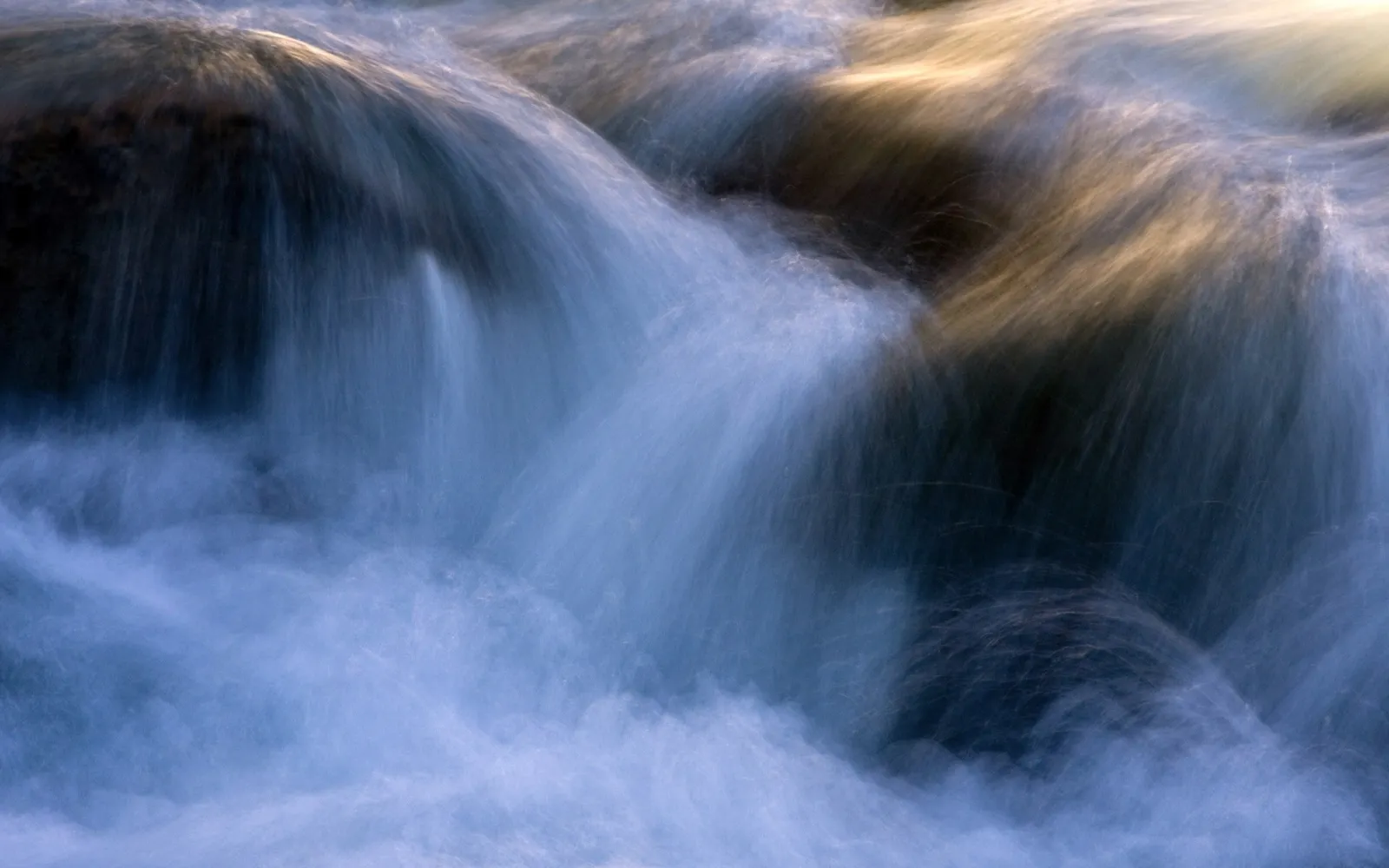 Close-up abstract view of water flowing rapidly over dark rocks, with streaks of light.