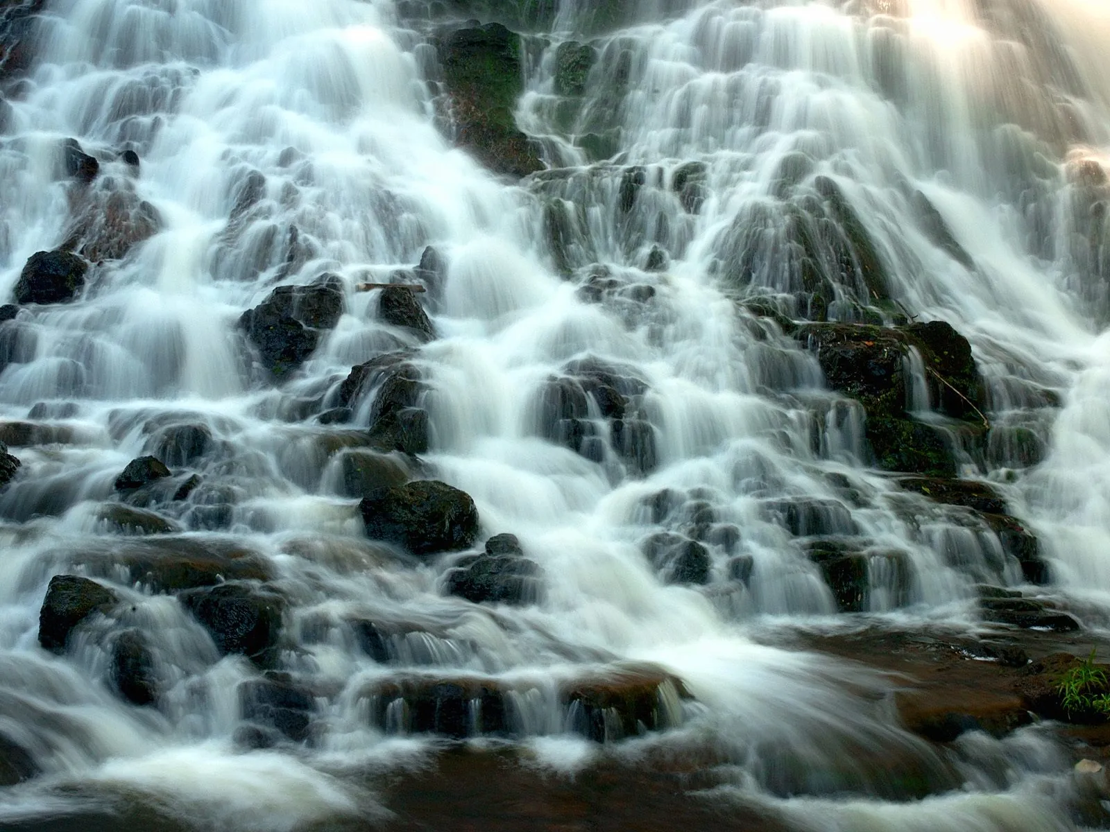 A close-up view of a multi-tiered waterfall with white water flowing over dark, mossy rocks.