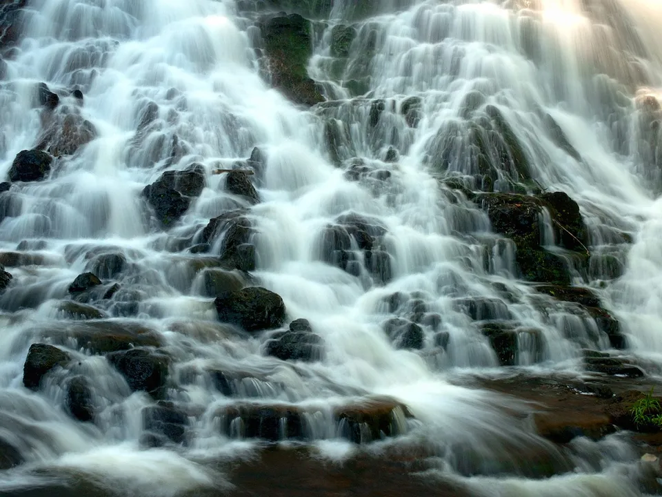 A close-up view of a multi-tiered waterfall with white water flowing over dark, mossy rocks.