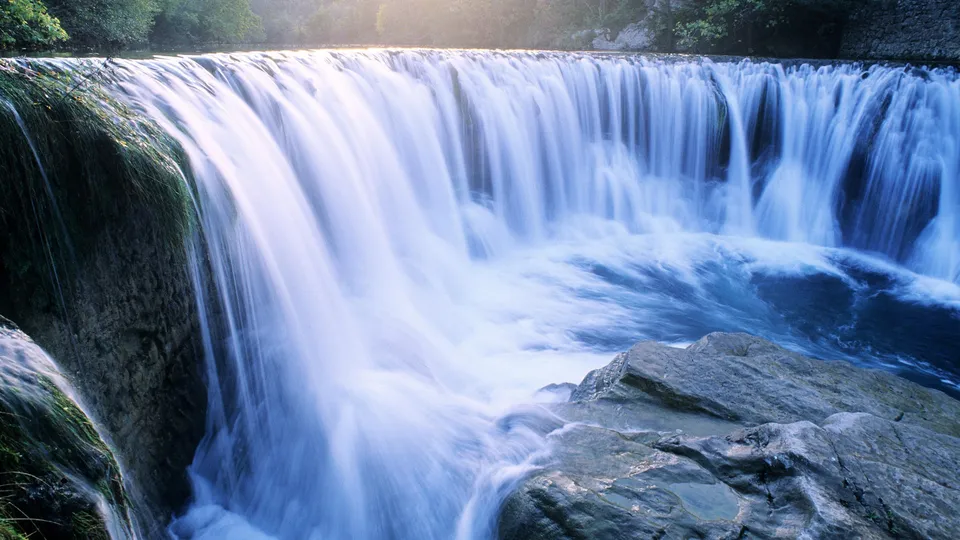 A wide waterfall cascades over rocks, with lush green foliage visible at the top.