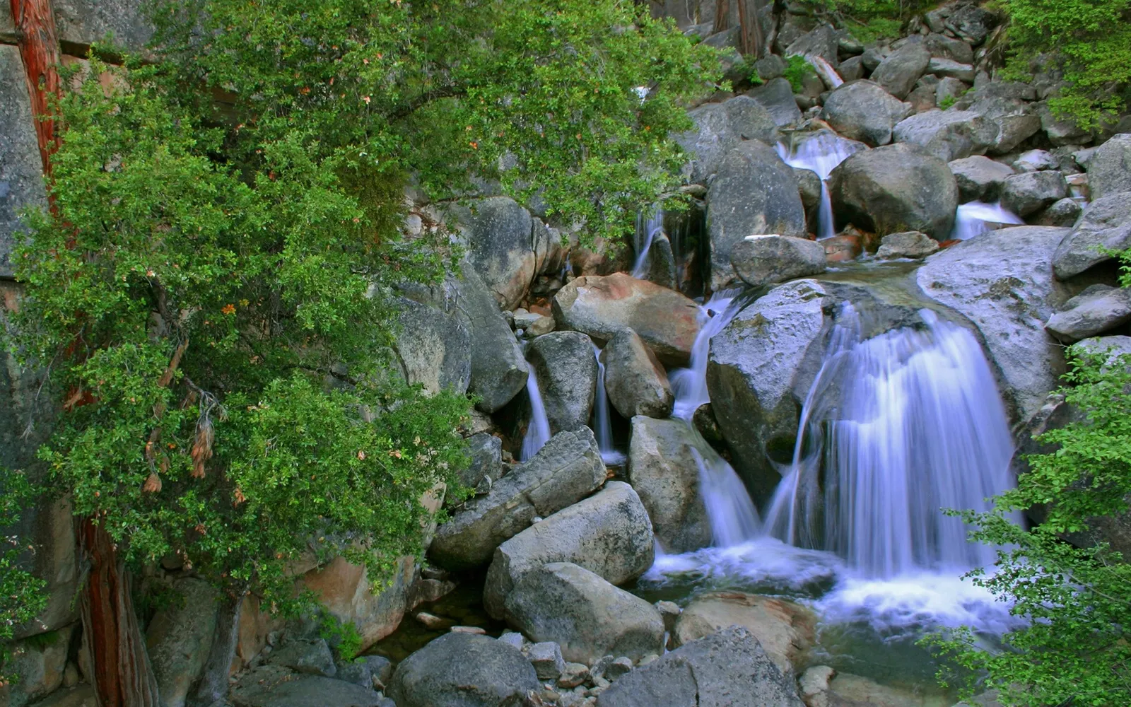 A small waterfall cascades over large, moss-covered boulders in a forest setting.