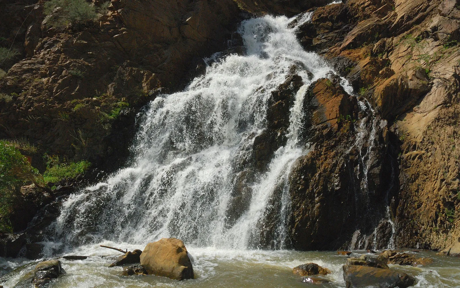 A powerful waterfall cascades down a steep, rocky mountainside into a churning river below.