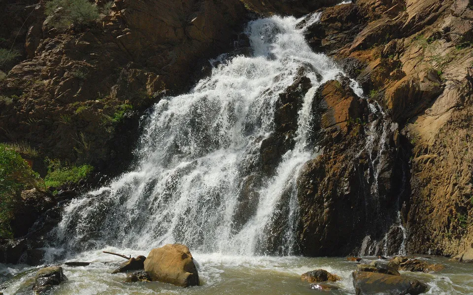 A powerful waterfall cascades down a steep, rocky mountainside into a churning river below.