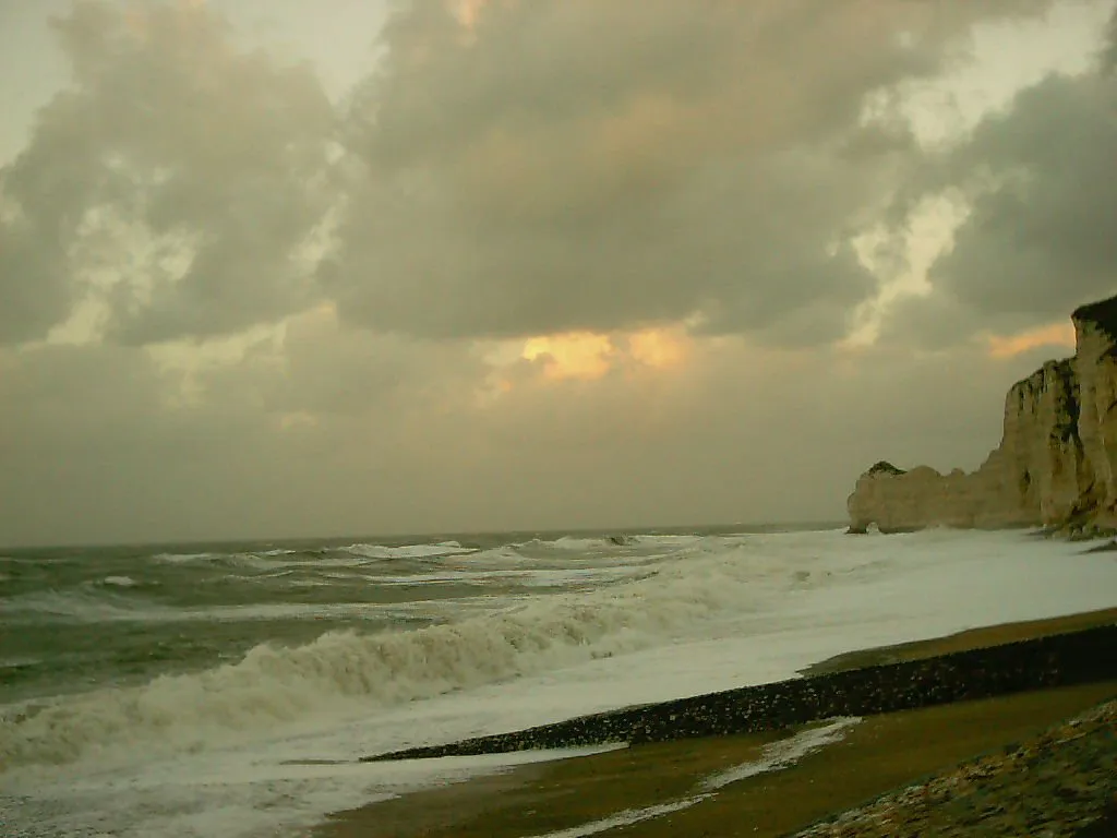 Waves crash against rugged white cliffs on a cloudy day.