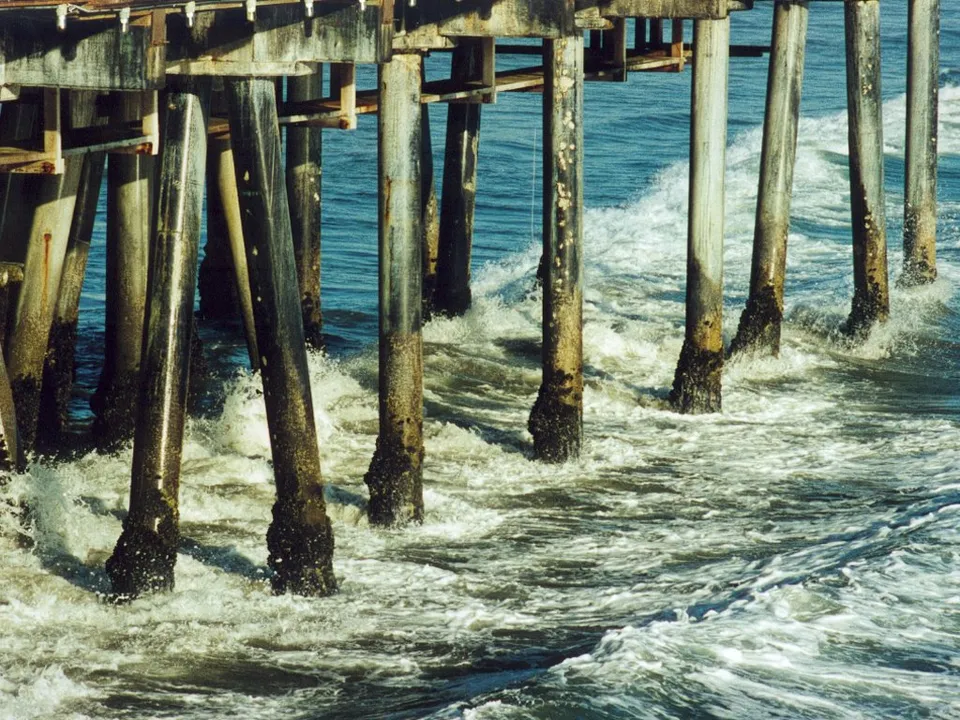Waves crash against the weathered wooden pilings of a pier extending over the ocean.