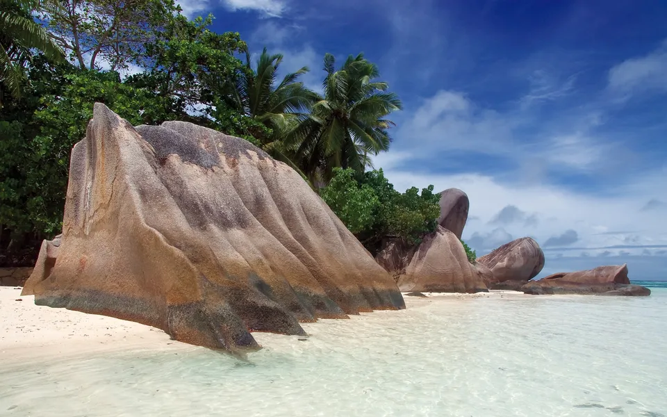 Massive granite boulders on a tropical beach with palm trees and blue sky.