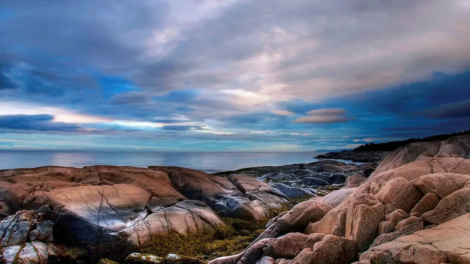 Rugged coastline with weathered rocks and a calm ocean under a dramatic sky.