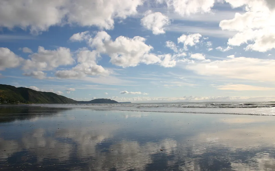 A wide, flat beach with wet sand reflecting the blue sky and white clouds.