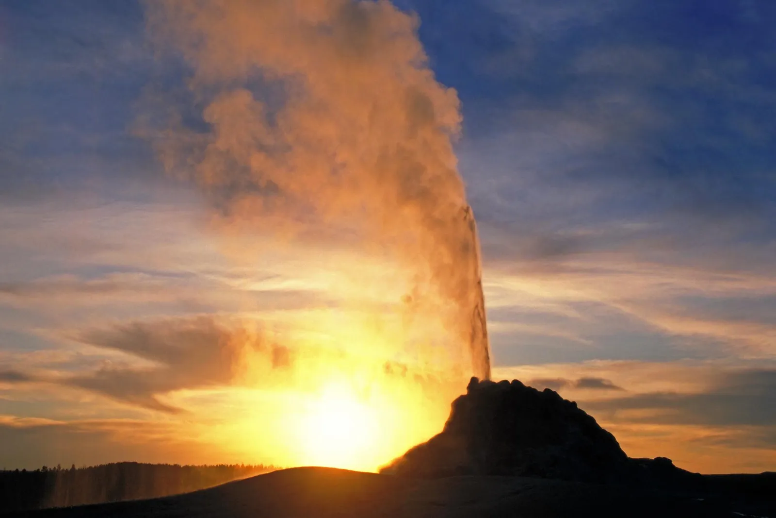 A geyser erupts with steam against a vibrant sunset sky.