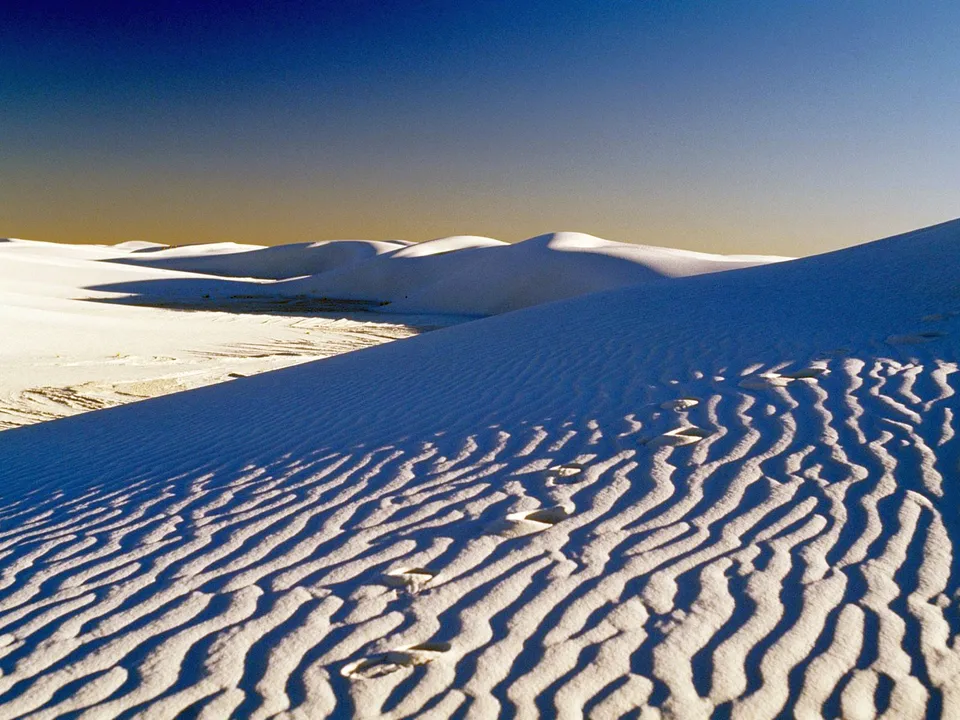 White sand dunes display ripples and footprints with long shadows.