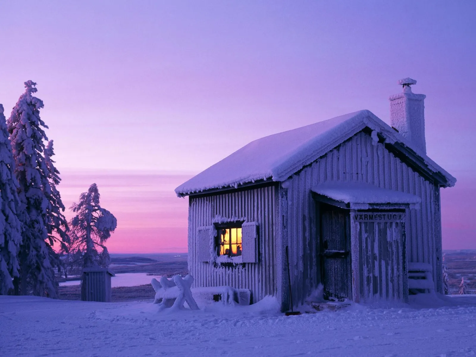 A snow-covered cabin with a warm light glowing from the window, set against a purple and pink twilight sky.