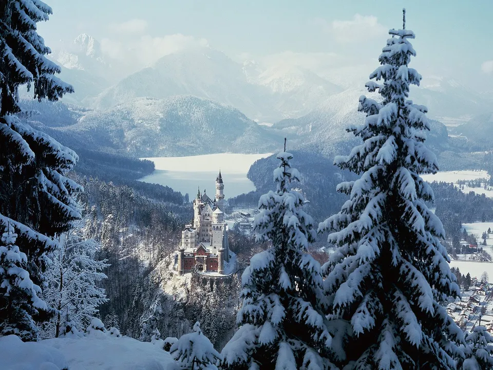A majestic castle sits atop a snow-covered hill, surrounded by wintery forests and mountains.