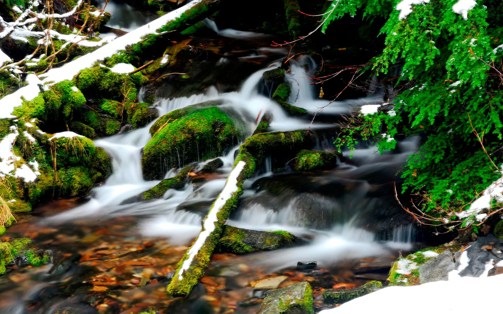 A long exposure shot of a stream with moss-covered rocks and snow.