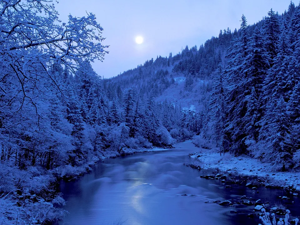 A wide river flows through a snow-covered forest under a pale moon.