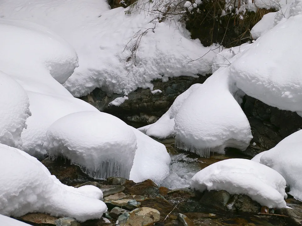 Close-up of snow-covered rocks with icicles hanging over a flowing stream in winter.