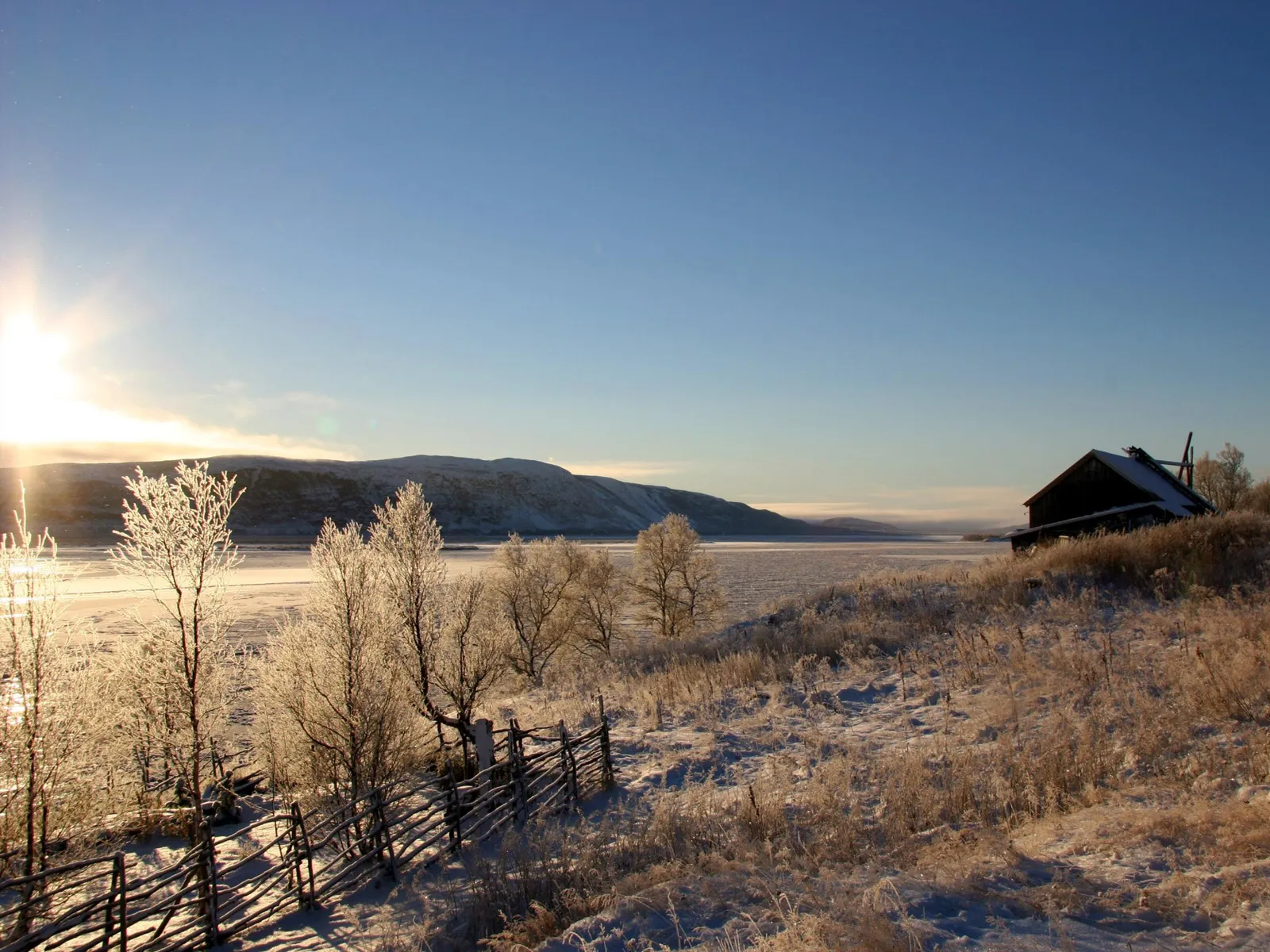 A frozen landscape bathed in the warm light of a sunrise, with a rustic barn on the right.