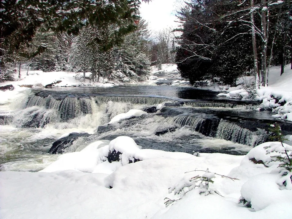 A wide waterfall cascades over rocks in a forest covered in snow.
