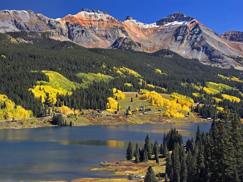 A mountain lake reflects the vibrant yellow aspen trees and dark green pine forests in autumn.