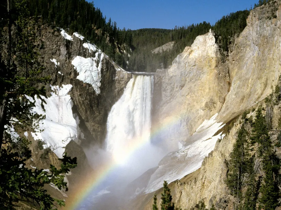 A powerful waterfall cascades down a rocky canyon, with a rainbow visible in the mist.