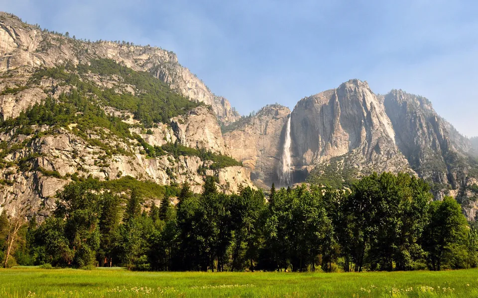 Yosemite Falls cascades down a granite cliff, framed by green trees and a meadow.