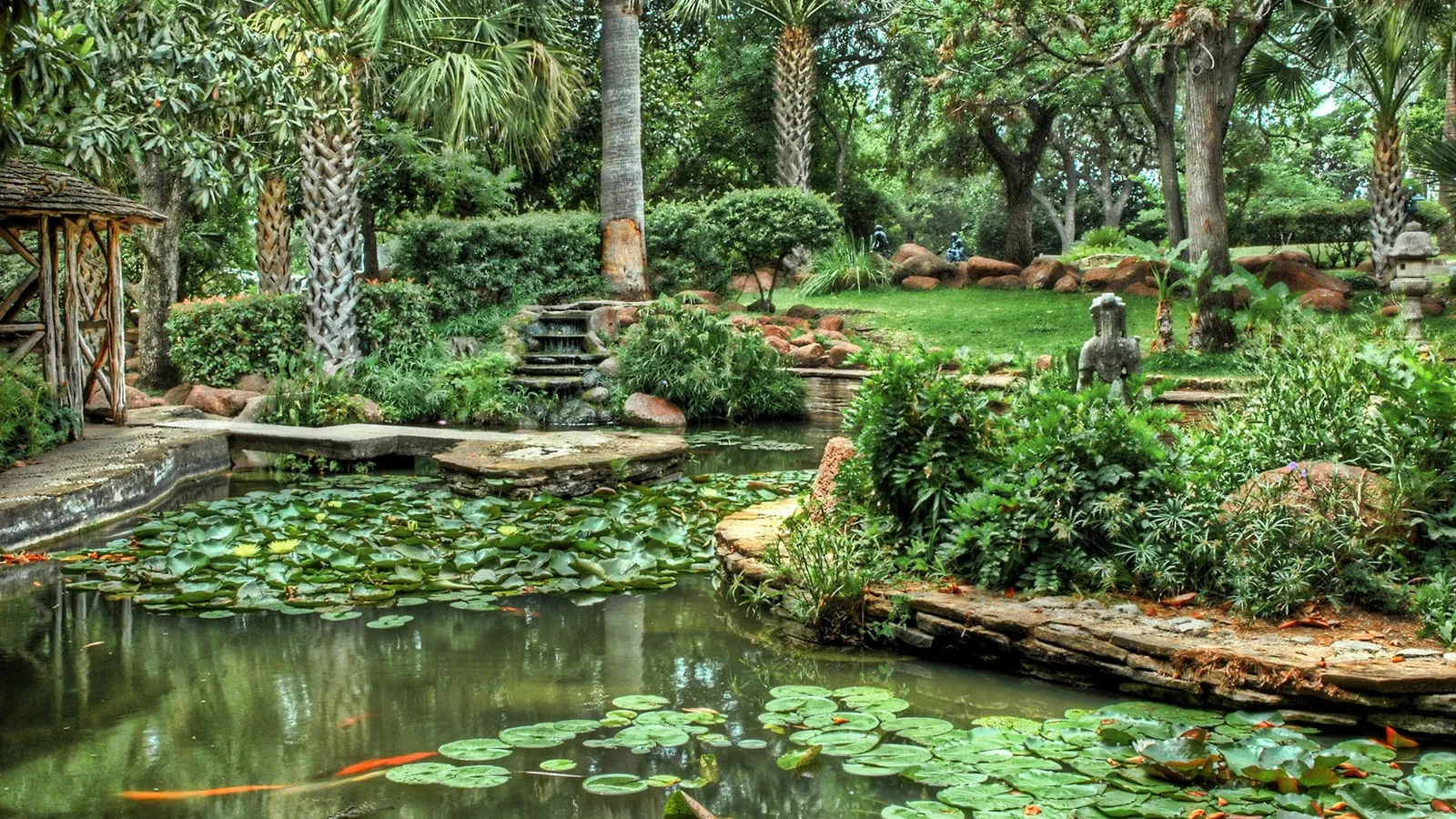 A serene garden pond filled with lily pads and koi fish, featuring a small waterfall and a wooden gazebo.